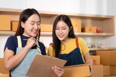 İki kadın, modern bir ofisteki kutularla çevrili bir panoda proje detaylarını incelerken arkadaşça bir tartışmaya giriştiler..