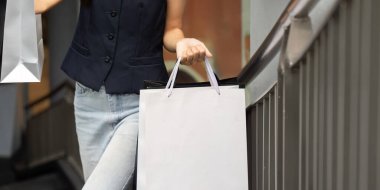 Şık bir kadın, elinde alışveriş torbalarıyla korkuluklara yaslanmış, Kara Cuma alışverişinin heyecanını yaşıyor..