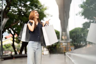 Mutlu bir kadın, başarılı bir Kara Cuma alışveriş çılgınlığından sonra alışveriş torbalarını tutarken heyecanla işaret eder..