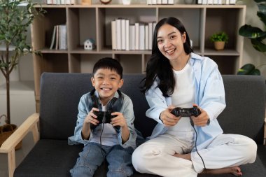 Bir anne ve oğul, video oyunları oynarken gülücüklerini ve heyecanlarını paylaşırlar. Modern bir evde aile eğlencesi ve bağlantılarını vurgularlar..