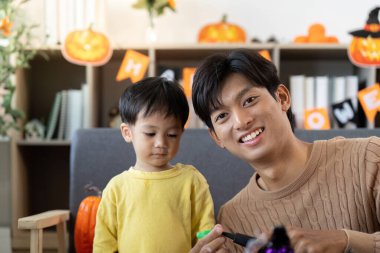 Neşeli bir baba ve oğul cadılar bayramı zanaatı yapıyor, balkabağı boyuyor ve dekore edilmiş bir oturma odasında kaliteli zaman geçiriyor..