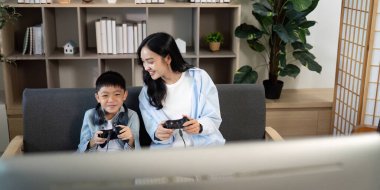 Bir anne ve oğlu keyifli bir oyun deneyimini paylaşıyor, kumandayı tutmak ve rahat bir oturma odasında video oyunları oynarken gülümsemek..