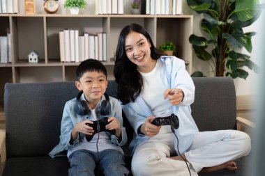 Bir anne ve oğul, kanepede eğlenceli bir oyun deneyimi paylaşıyor, sıcak bir evde aile bağlarının ve eğlencenin altını çiziyor..