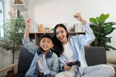 Neşeli anne ve oğul, evde video oyunu oynarken, aile bağlarını ve mutluluğu sergileyerek muzaffer bir anı paylaşıyorlar..