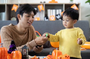 Bir baba ve oğul Cadılar Bayramı şenliklerine katılır, balkabaklarını boyar ve süslü bir alanda kahkahalarını paylaşırlar..