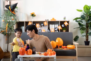 Neşeli bir baba ve oğul Cadılar Bayramı aktivitelerine katılıyor, balkabaklarını süslüyor ve sıcak bir yuva ortamında kahkahalarını paylaşıyorlar..