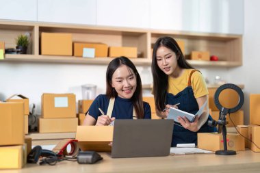 Stratejileri tartışan iki girişimci, iyi organize edilmiş bir ev ofisinde envanter işletirken, işbirliği ve odaklanma sergiliyorlar..