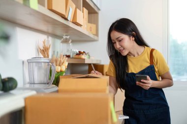 Konforlu bir ev ofisinde paketleri yönetirken, üretkenlik ve organizasyon sergileyen odaklı bir girişimci notlar yazıyor..