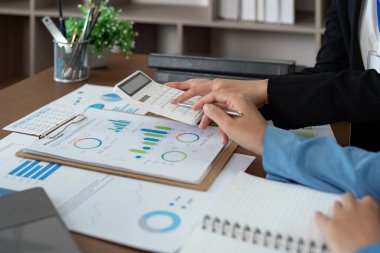 Mali danışman, bir ofis ortamında mali verileri analiz etmek için hesap makinesi ve grafikler kullanarak bir müşteriyle işbirliği yapar..