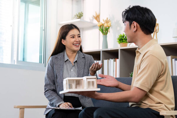 A smiling real estate agent engages with a client, presenting a model home in a bright, inviting office environment.