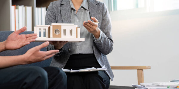A real estate agent holds a model home while discussing its features with a client in a contemporary office space.