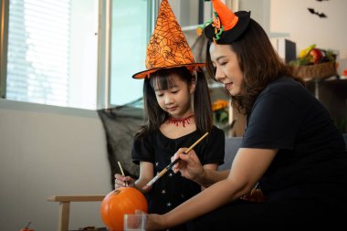 Bir anne ve kız Cadılar Bayramı zanaat seansının keyfini çıkarırlar, balkabaklarını boyarlar ve kostümleriyle gülümsemelerini paylaşırlar..