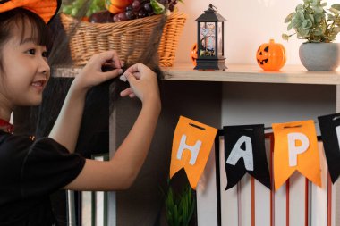 Bayram ruhunu kucaklayan, bayram süslemeleriyle çevrili bir kız neşeyle bir Cadılar Bayramı afişi asıyor..