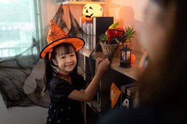 Cadı şapkalı neşeli bir kız Cadılar Bayramı süslerini düzenliyor, bayramın ruhunu somutlaştırıyor..