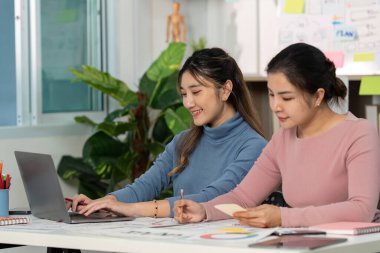 UX ve UI tasarımı üzerinde işbirliği yapan iki tasarımcı, proje fikirlerini geliştirmek için bir dizüstü bilgisayar ve yaratıcı materyal kullanıyorlar.