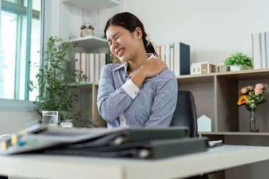 Ofis masasında omzunu tutarken acı çeken bir kadın ofis sendromunun etkilerini vurguluyor..