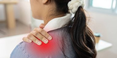 Ofis ortamındaki genç bir kadın omzunu rahatsızlık içinde tutuyor ve ofis sendromunun sağlık ve verimlilik üzerindeki etkisini gösteriyor..