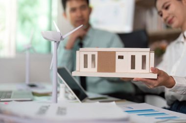 Bir profesyonel, sürdürülebilir tasarım ve yenilenebilir enerji kavramlarını vurgulayan çevre dostu bir evin modelini sunar.