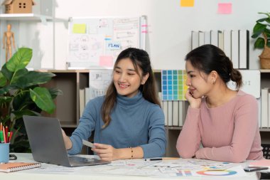 İki kadın tasarımcı UX ve UI tasarımı hakkında bir tartışmada bulundu, bir dizüstü bilgisayardaki çizimleri ve dijital kavramları gözden geçirdi..
