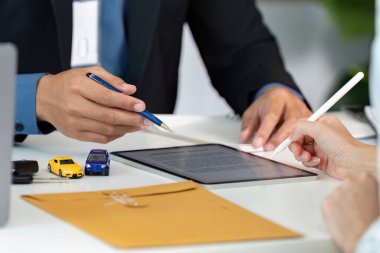 Bir sigorta acentesi, bir müşteriye tablet ve minyatür arabaları illüstrasyon için kullanarak araba sigortası poliçesini açıklar..