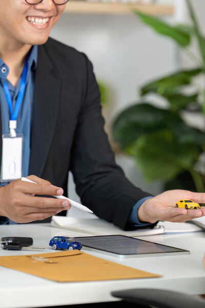 A friendly insurance agent smiles while discussing car insurance options, using toy cars as props for clarity.