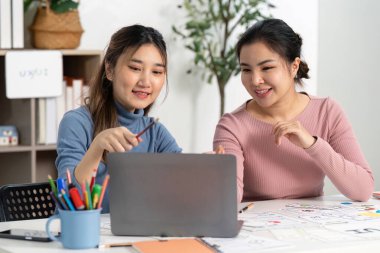 UX ve UI projelerinde işbirliği yapan iki tasarımcı, modern bir çalışma alanında dizüstü bilgisayar üzerinde çalışırken fikir ve çizimleri paylaşıyorlar..