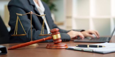 Bir dizüstü bilgisayarda hukukçu tipler otururken, masanın üzerinde bir tokmak ve adalet terazisi belirgin bir şekilde sergileniyor..