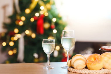 Two glasses of sparkling drink beside a plate of pastries, set against a backdrop of a glowing Christmas tree.