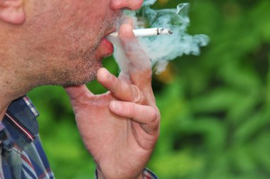 Genç adam dışarıda zevkle sigara içiyor. 