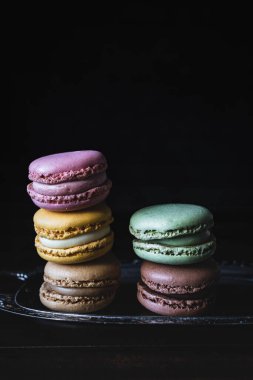 Gümüş tepside renkli makaron yığını ve koyu arka plan