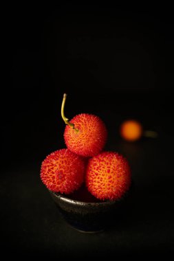 Arbutus, çilek ağacının meyvesi, siyah arkaplanı ve fotokopi alanı var. Kaba dokulu olgun yabanmersini.