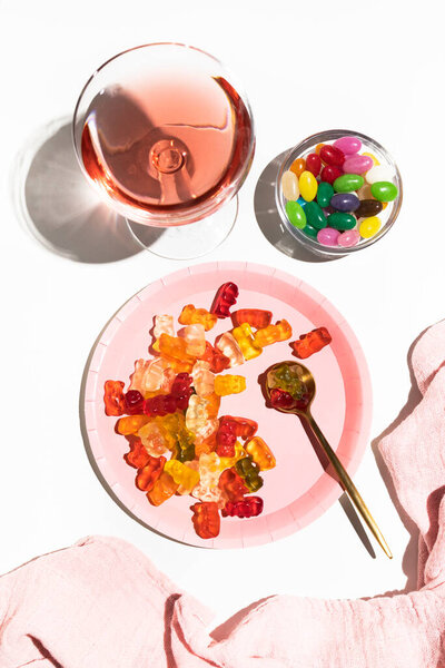 Plate with gummy bears, jelly beans and a glass with a pink drink. Coloring in food. Parties and celebrations