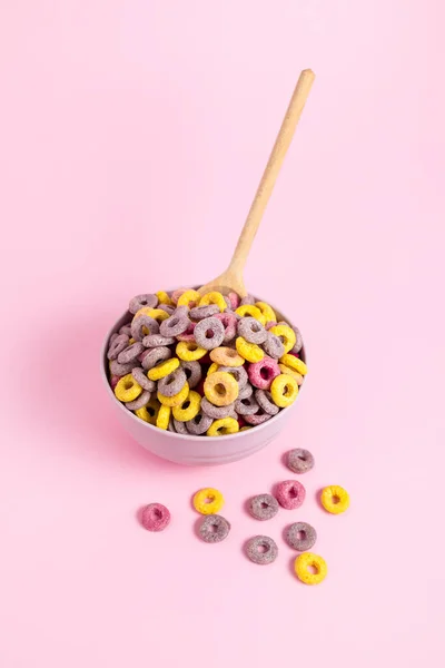 Bowl of colorful cereal with a spoon on a pink background