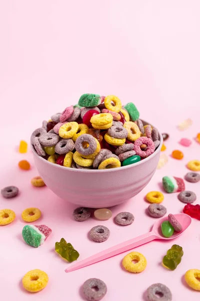 A bowl of cereal and candies with a pink spoon on a pink background
