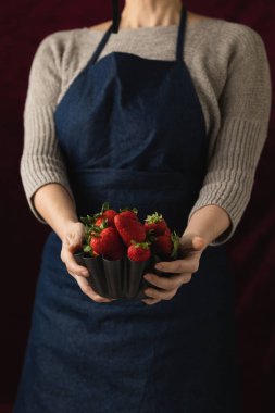 Elinde olgun, yenmeye hazır kırmızı çileklerle dolu metal bir kase tutan bir kadın.