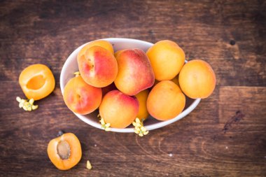 Bahçedeki ahşap bir masada olgun kayısılarla beyaz seramik kase.