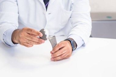 Bir ortopedik cerrahın ellerinin kalça protezini tutarken ve gösterirken yakın plan görüntüsü. Tıbbi ve sağlıkla ilgili konular için ideal.