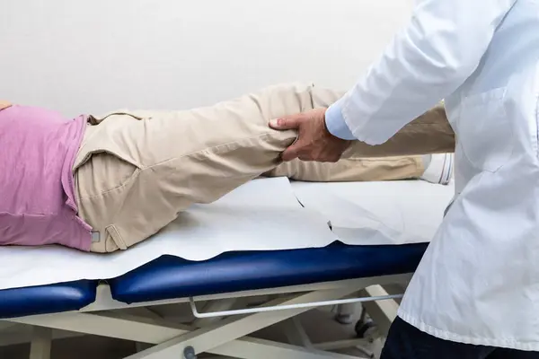 stock image A doctor in a white coat examining a patient's knee during a medical consultation in a clinical setting.