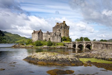Loch Duich tarafındaki Eilean Donan Kalesi manzaralı, yemyeşil ve sakin bir göl ile çevrili.