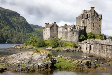 Loch Duich tarafındaki Eilean Donan Kalesi manzaralı, yemyeşil ve sakin bir göl ile çevrili.