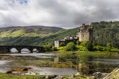 Loch Duich tarafındaki Eilean Donan Kalesi manzaralı, yemyeşil ve sakin bir göl ile çevrili.