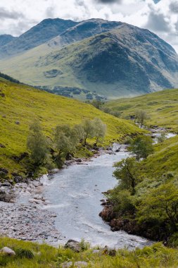 Bereketli, yemyeşil Glencoe Vadisi 'nde, arka planda yüksek dağlar olan sakin bir nehir esiyor..