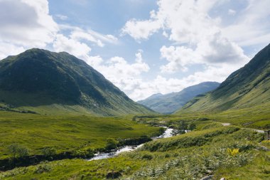 Bereketli, yemyeşil Glencoe Vadisi 'nde, arka planda yüksek dağlar olan sakin bir nehir esiyor..