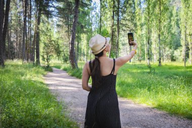 Rio Lobos Canyon, Soria, İspanya 'nın sakin ortamında bir orman yolunda dururken cep telefonuyla fotoğraf çeken bir kadın..