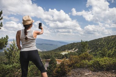 Bir kadın, İspanya, Soria 'daki Neila Gölleri' nin manzarasını seyrediyor, akıllı telefonuyla anı yakalıyor..