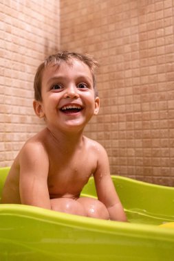 Banyoda banyo yaparken eğlenen ve gülümseyen bir çocuğun neşeli bir banyo deneyimini yakaladığı neşeli bir an.