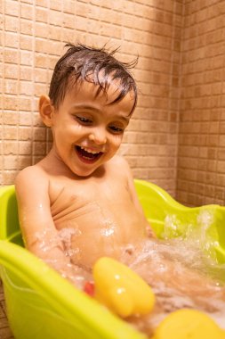 Banyoda banyo yaparken eğlenen ve gülümseyen bir çocuğun neşeli bir banyo deneyimini yakaladığı neşeli bir an.