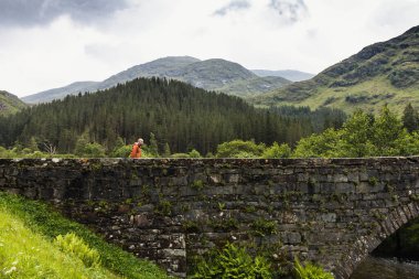 İskoç İskoçya 'sında Glen Shiel' in güzel yeşil manzarası, üzerinde uzak bir adamın durduğu taş bir köprü, doğal ortama uyum sağlıyor.