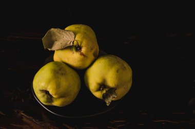 Yeni toplanmış ayva yavrularının dramatik durgun hayatı, gösterişsiz bir ışık altında çekiliyor, zengin dokuları ve meyvenin doğal güzelliğini vurguluyor.