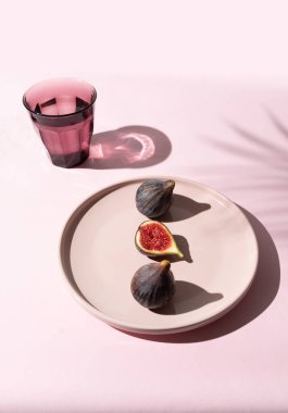 Pembe bir arka planda pembe bir tabakta iki incirin yanında mor bir incir kesiği. Taze ve canlı.